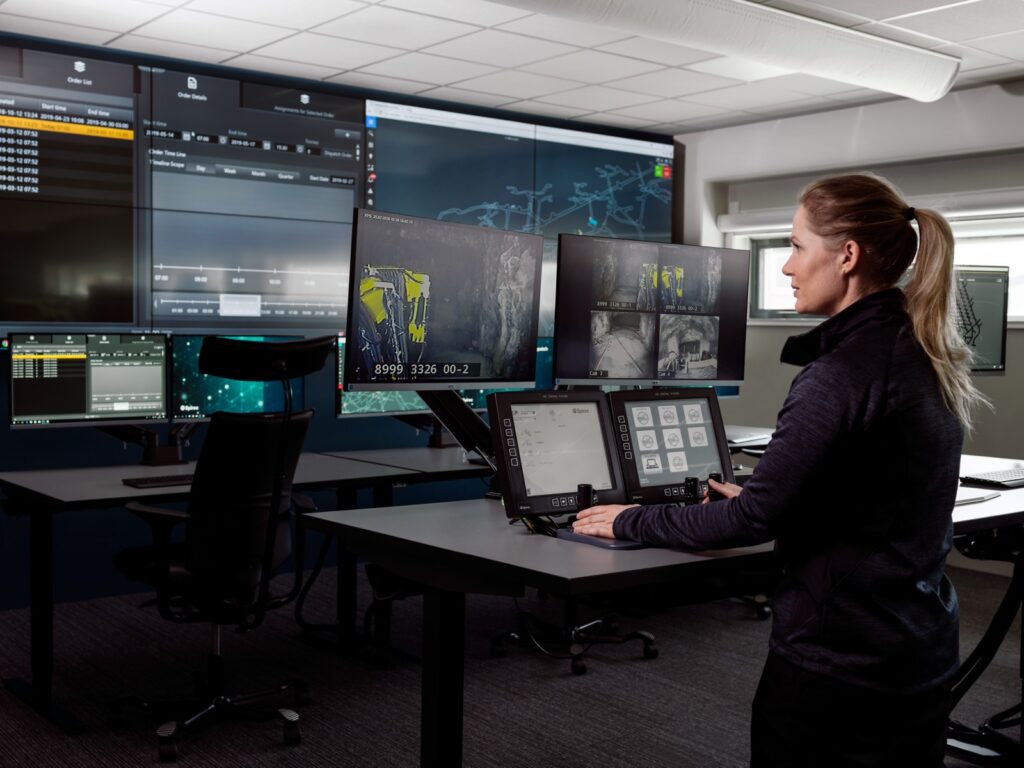 En kvinna står vid en kontrollpanel med många skärmar