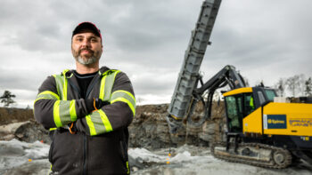 En operatör står i en bergtäkt med en borrigg från Epiroc i bakgrunden